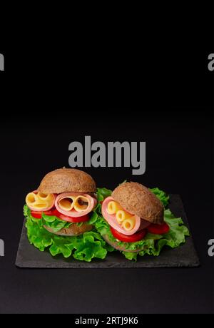 Appetizing sandwich features ham, cheese, and fresh lettuce served on a dark background. Vertical banner Stock Photo