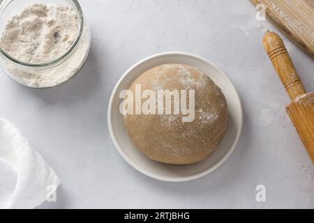 Rye dough for pies, rye flour and rolling pin on a gray background, top view. Cooking stage. Stock Photo