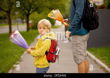 Sad little child,. holding fathers hand, going to school crying, caring bouquets of flowers for teachers, going to preschool Stock Photo