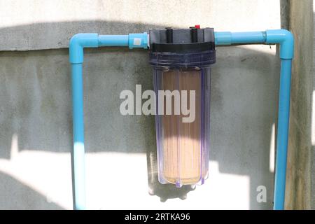 The single stage water filter is mounted on a blue PVC plastic water pipe that is attached to the wall. Stock Photo