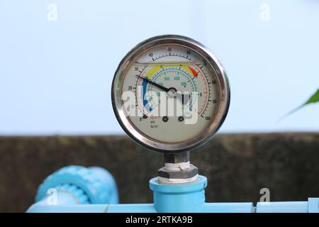 Circular water pressure meter attached to blue PVC water pipe to measure tap water pressure. Stock Photo
