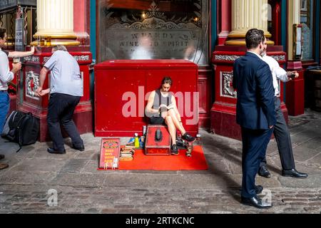 A Female Shoe Shiner Reads A Book Whilst Waiting For Customers, Leadenhall Market, City of London, London, UK. Stock Photo