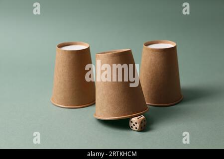 Three paper cups and dice on pale olive background. Thimblerig game ...