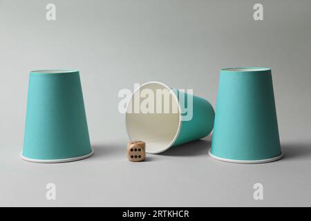 Three paper cups and dice on light blue background, closeup. Thimblerig ...