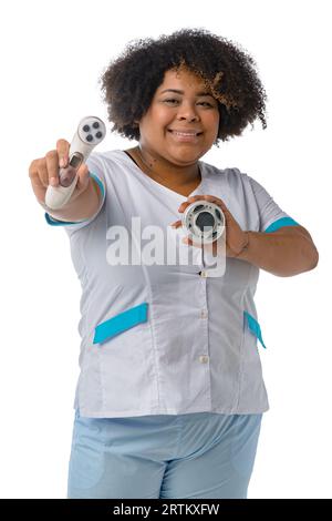vertical image young afro latina beautician woman wearing uniform, standing looking at camera smiling and showing her skin cleaning work tools Stock Photo