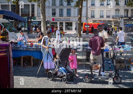 A woman of African origin stands with her young daughter and holds a broom and a pushchair as she browses stalls outside the Central Market  (Marche d Stock Photo