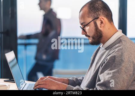 Young businessman working on laptop in office. Portrait of IT software engineer in glasses, side view. Stock Photo