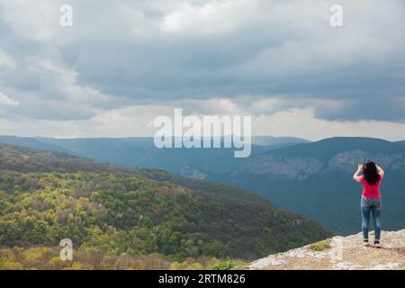 a woman stands on a mountain and photographs nature hiking journey Stock Photo