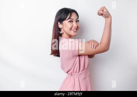 Excited Asian woman wearing a pink blouse showing strong gesture by lifting her arms and muscles smiling proudly Stock Photo