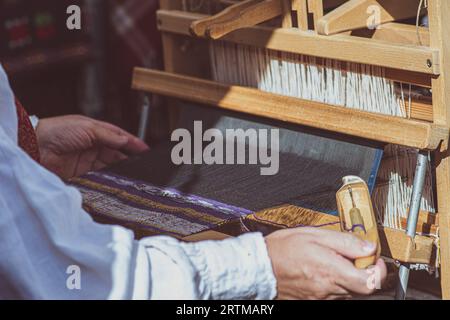 A craftswoman working on an ancient wooden weaving loom in traditional dress in an arts and crafts fair in Vilnius, Lithuania Stock Photo