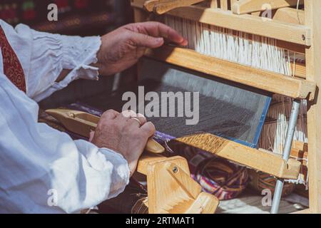 A craftswoman working on an ancient wooden weaving loom in traditional dress in an arts and crafts fair in Vilnius, Lithuania Stock Photo