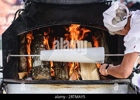 Woman preparing a tree cake, Lithuanian šakotis, Polish sękacz, Belarusian bankucha, German baumkuchen, cooked over an open fire Stock Photo