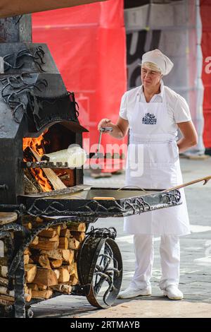 Woman preparing a tree cake, Lithuanian šakotis, Polish sękacz, Belarusian bankucha, German baumkuchen, cooked over an open fire, vertical Stock Photo