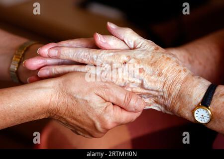Retirment home.  Close up of care assistants hand reassuring senior woman. Stock Photo