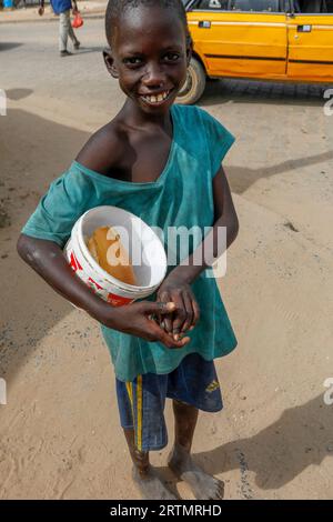 Smiling talibe (Koranic school pupil) with begging bucket looking at camera in Fatick, Senegal Stock Photo