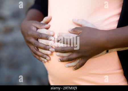 White man hugging pregnant black woman. Le Mesnil en Ouche, France. Close-up on hands and belly Stock Photo