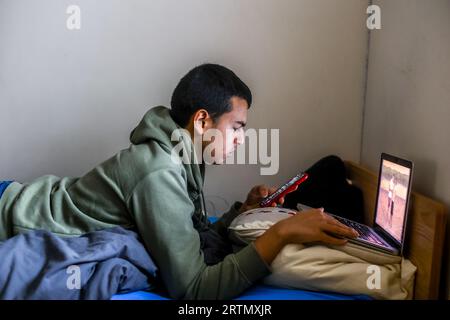 Teenager lying on his bed and using a laptop and a cell phone in Montrouge, France Stock Photo