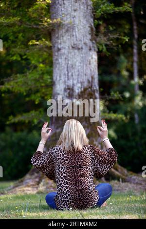 Woman sitting in a forest meditating, practicing yoga. Stock Photo