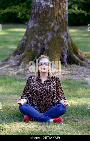 Woman sitting in a forest meditating, practicing yoga. Stock Photo