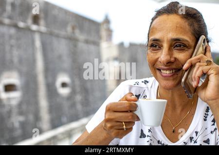 Smiling woman using a cell phone and drinking coffee in Dubrovnik, Croatia Stock Photo