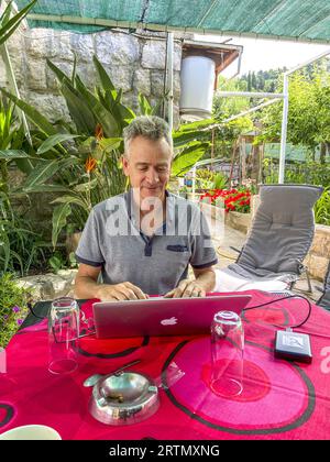 Man using a laptop on a table on a terrace with garden in Dubrovnik,  Croatia Stock Photo