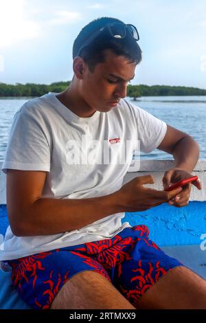 Young man using a cell phone on a boat cruising in the Saloum river delta, Senegal Stock Photo