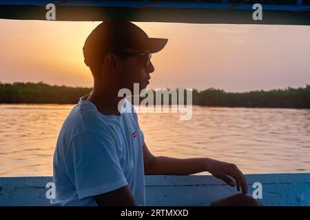 Young man on a boat cruising in the Saloum river delta at dusk, Senegal Stock Photo