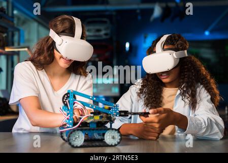 Two young women in VR glasses doing experiments in robotics in a laboratory. Robot on the table Stock Photo