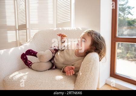 Dreamy cute little girl in stylish warm winter clothes, posing outdoors in  the snowy forest and looking up. Pretty child girl in pink outfit enjoying  winter season and snow in the nature