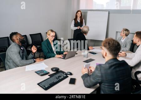 Wide shot of businesswoman company representative present to diverse client investors. Female business coach teaching multi-ethnic trainees during Stock Photo