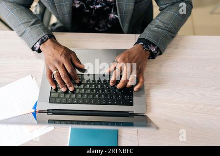 Closeup top view of unrecognizable African businessman typing on laptop at home office, web surfing information in internet, working distantly online Stock Photo