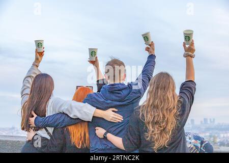 Group of 4 young people, 3 girls and 1 guy hold up Starbucks cups, taken from behind.  No faces. Stock Photo