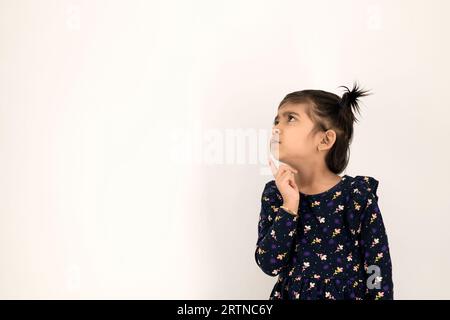 Thoughtful beautiful little girl with serious eye and face, thinking, hesitate or have an intelligent idea or solution, with isolated white background Stock Photo