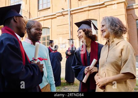 Parents congratulating their children with graduation of university while they standing outdoors Stock Photo