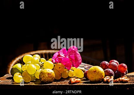 grapes, figs and nuts with a beautiful purple flower lie on a wooden board illuminated by the sun Stock Photo