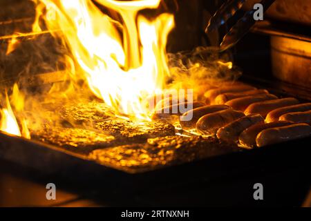 Sausages and burgers meat BBQ cooking on grill outdoors with big orange fire flames. Delicious food. Stock Photo
