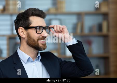 Close up portrait of mature successful businessman, man inside home office in business suit looking towards window, satisfied with achievement results boss with beard. Stock Photo