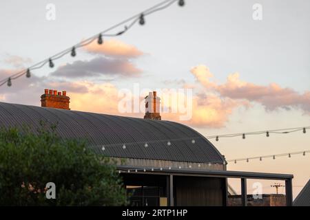 Beautiful sunset over old cow shed barn roof in countryside with chimneys and clouds in view. Stock Photo