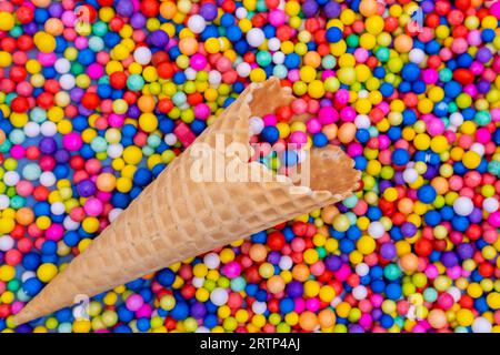 An empty waffle cone with scattered multicolored round candies, dragees. A fun holiday. Children's sweets. Festive cheerful background. Stock Photo