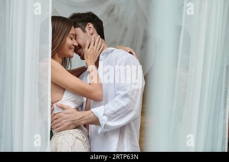 happy couple before kiss, handsome man embracing woman near white tulle of private pavilion Stock Photo