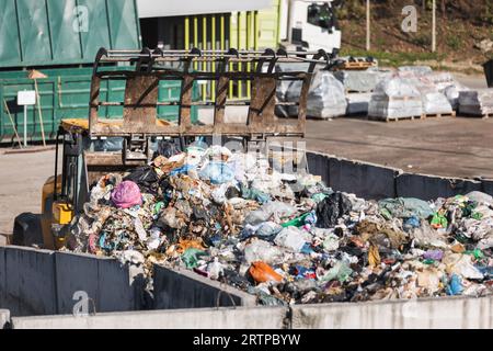 Yellow skid steer loader moving wooden waste material, shaking out a scrap grapple on the garbage heap in the materials recovery facility Stock Photo