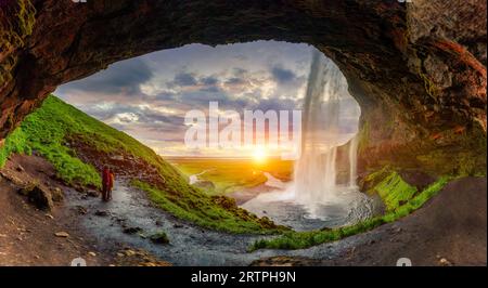 Majestic natural cave with sunset over Seljalandsfoss waterfall flowing and tourist enjoying in summer at South of Iceland Stock Photo