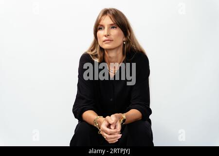 Portrait of attractive mature woman in black wear model showing golden bracelets, rings, chains on white background. Stock Photo