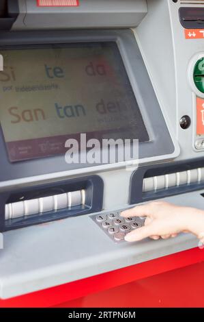 Viladecans, Spain - September 12, 2023: Santander bank ATM with its advertising on the screen and a woman's hand putting the pin. Stock Photo