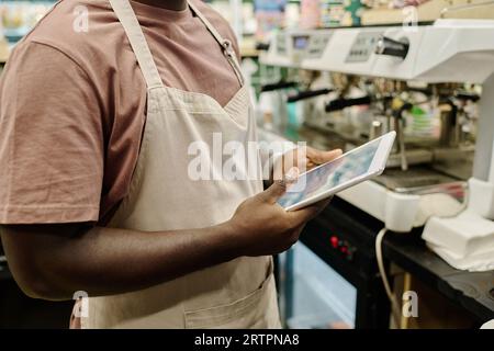 Close-up of bartender in apron working online on tablet pc in cafe Stock Photo