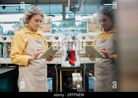 Saleswoman in apron using digital tablet while working in supermarket Stock Photo