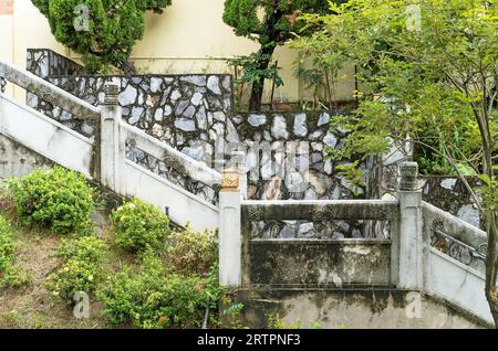 Old stone wall with concrete staircase surrounded by trees in an oriental garden in Hong Kong Stock Photo