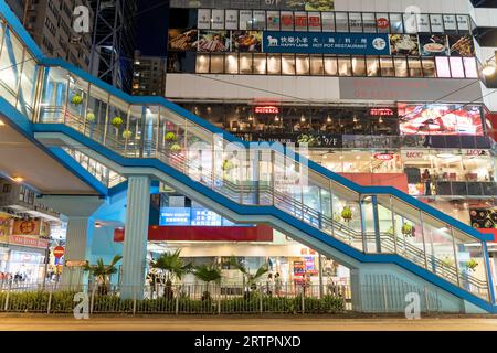 Blue stairway leading up to a pedestrian walkway in front of shops and restaurants in Causeway Bay at night. Hong Kong - 28th August 2023 Stock Photo