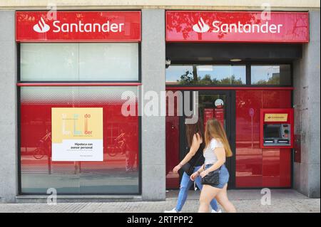 Viladecans, Spain - September 12, 2023: Two unrecognizable young women passing and looking at a Santader bank branch on a sunny day. Stock Photo