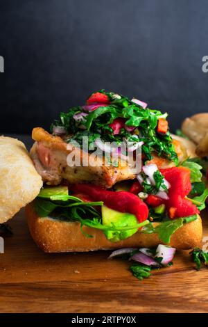 Chimichurri Chicken Sandwich on a Wooden Cutting Board: Open-faced sandwich topped with avocado, roasted peppers and arugula Stock Photo